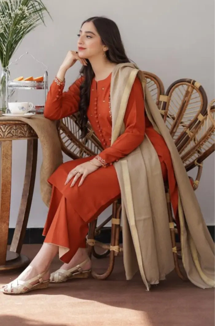 Woman in an orange outfit with a beige scarf sitting on a wooden chair.