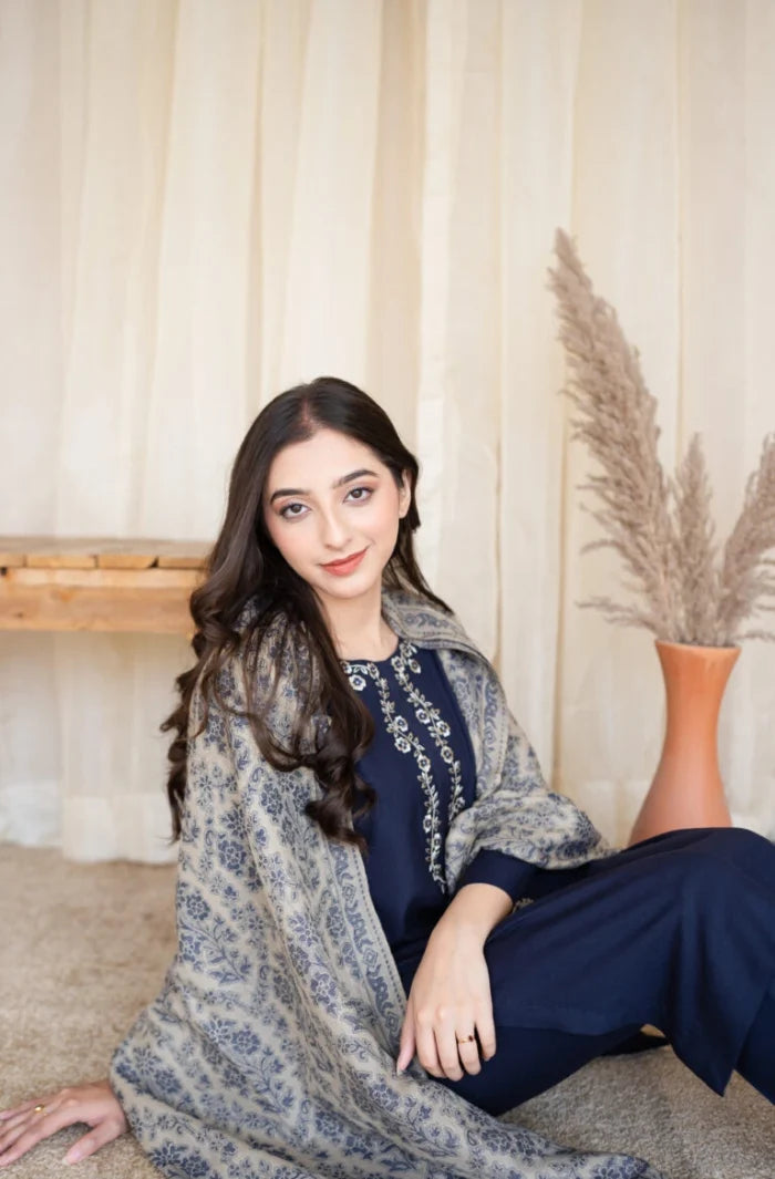 Woman sitting on the floor wearing a floral shawl and dark outfit with a neutral background